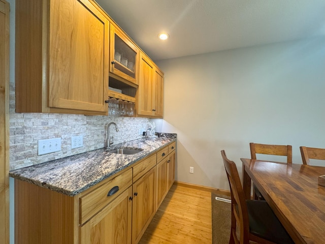 25797 Silver Beach Rd, Minnewaska Twp, MN 56334 - kitchen featuring a sink, decorative backsplash, dark stone counters, light wood-type flooring, and glass insert cabinets