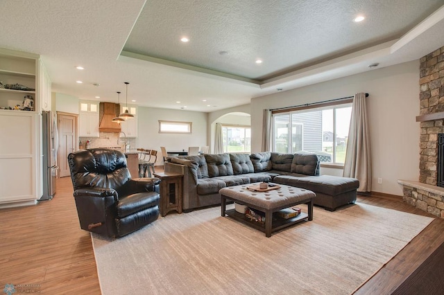 1908 65th Ave S, Fargo, ND 58104 - living area featuring a fireplace, a raised ceiling, light wood-type flooring, a textured ceiling, and arched walkways
