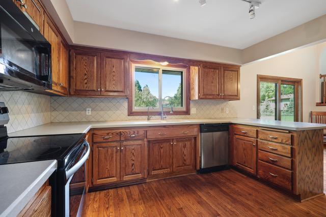 720 Tanglewood Dr, Shoreview, MN 55126 - kitchen featuring appliances with stainless steel finishes, a peninsula, a sink, light countertops, and dark wood-type flooring