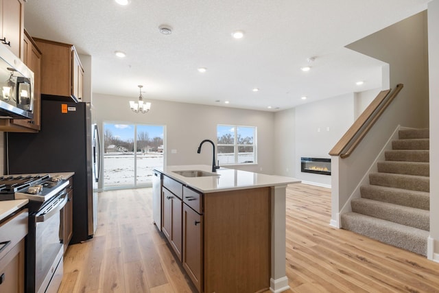 23221 Creekview Ct, Rogers, MN 55374 - kitchen featuring a sink, stainless steel appliances, a glass covered fireplace, light wood-style flooring, and a chandelier