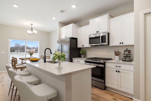 23225 Creekview Ct, Rogers, MN 55374 - kitchen with stainless steel appliances, a sink, light wood-type flooring, backsplash, and an island with sink