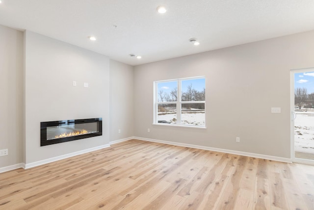 23225 Creekview Ct, Rogers, MN 55374 - unfurnished living room featuring a glass covered fireplace, light wood-type flooring, recessed lighting, and baseboards