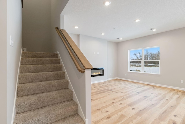 23225 Creekview Ct, Rogers, MN 55374 - staircase featuring wood finished floors, a glass covered fireplace, recessed lighting, and baseboards