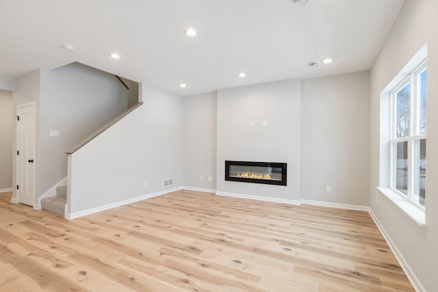 23225 Creekview Ct, Rogers, MN 55374 - unfurnished living room featuring light wood-style floors, stairway, a glass covered fireplace, and recessed lighting