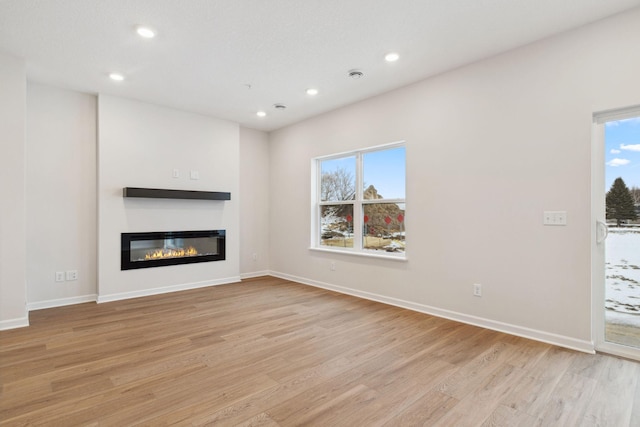23229 Creekview Ct, Rogers, MN 55374 - unfurnished living room with light wood-style flooring, a glass covered fireplace, recessed lighting, healthy amount of natural light, and baseboards