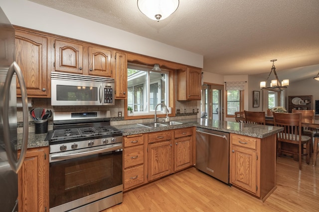 8821 Jonquil Ln N, Maple Grove, MN 55369 - kitchen with stainless steel appliances, a peninsula, light wood-type flooring, a textured ceiling, and brown cabinets