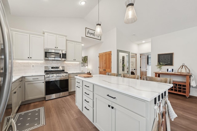 25822 Emerson Ct, Wyoming, MN 55092 - kitchen featuring appliances with stainless steel finishes, tasteful backsplash, dark wood-style flooring, a center island, and light stone countertops