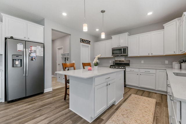 12905 Jewell Cir NE, Blaine, MN 55449 - kitchen featuring stainless steel appliances, white cabinetry, wood finished floors, a center island, and a kitchen breakfast bar