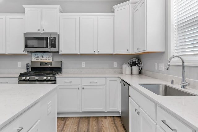 12905 Jewell Cir NE, Blaine, MN 55449 - kitchen with stainless steel appliances, a sink, white cabinetry, light stone counters, and wood finished floors
