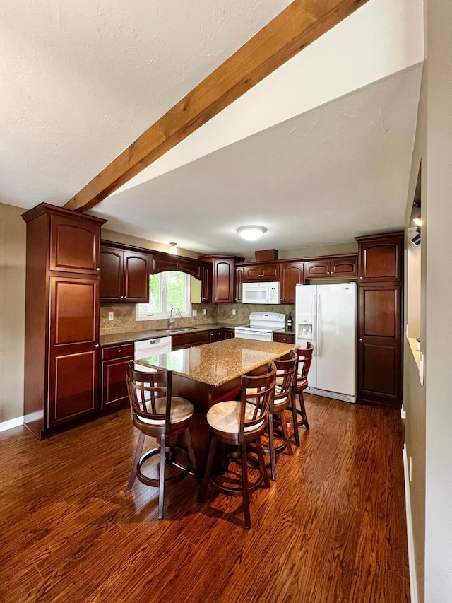 17300 Baseline Ave, Sand Creek Twp, MN 55352 - kitchen featuring white appliances, dark wood-type flooring, beam ceiling, a kitchen island, and backsplash