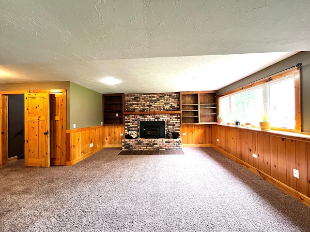 17300 Baseline Ave, Sand Creek Twp, MN 55352 - unfurnished living room featuring a textured ceiling, wood walls, wainscoting, a fireplace, and carpet floors