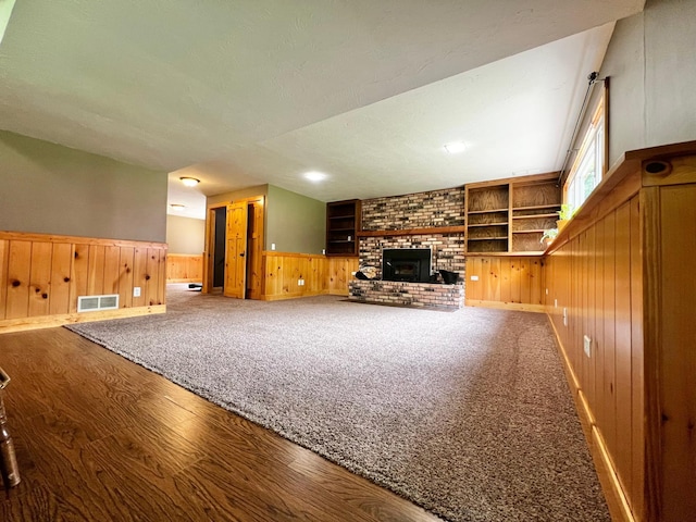 17300 Baseline Ave, Sand Creek Twp, MN 55352 - unfurnished living room featuring wooden walls, wood finished floors, a brick fireplace, built in features, and a wainscoted wall