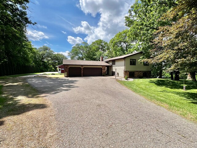 17300 Baseline Ave, Sand Creek Twp, MN 55352 - split level home with driveway, an attached garage, a front lawn, stone siding, and a chimney