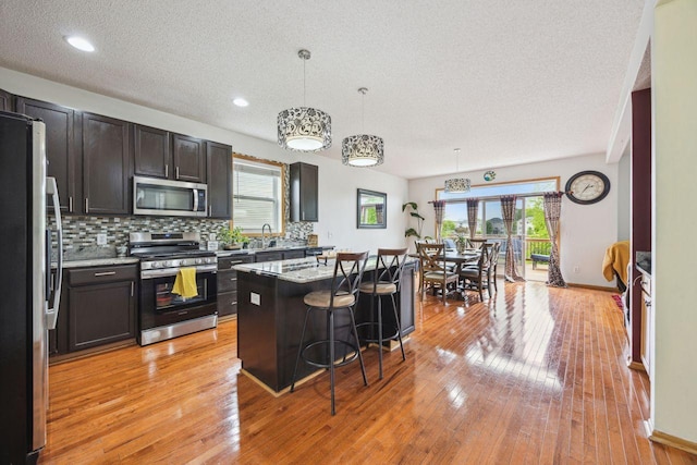 12332 3rd St NE, Blaine, MN 55434 - kitchen featuring stainless steel appliances, a sink, a breakfast bar, light wood finished floors, and a textured ceiling