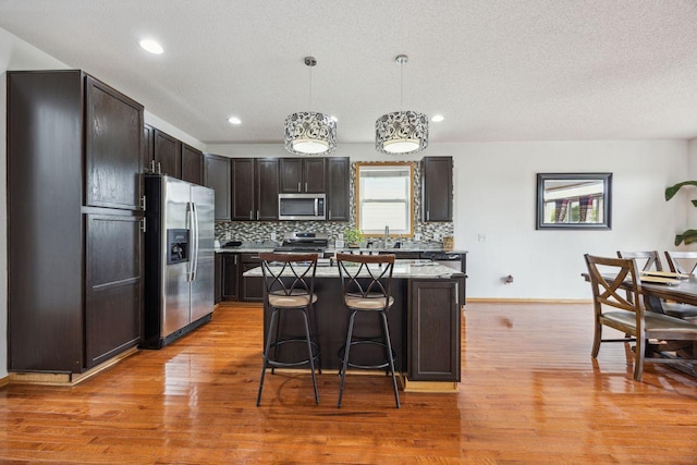 12332 3rd St NE, Blaine, MN 55434 - kitchen with appliances with stainless steel finishes, light wood finished floors, tasteful backsplash, a breakfast bar area, and recessed lighting