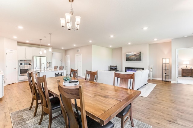 19171 Cottage Rd, Farmington, MN 55024 - dining room with light wood-style flooring, recessed lighting, a chandelier, baseboards, and a glass covered fireplace
