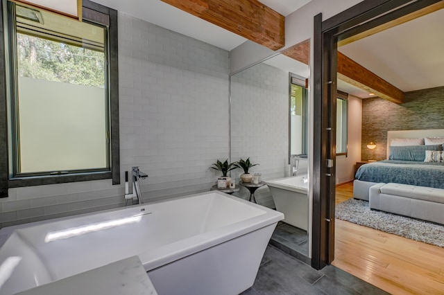 120 Eastbank Ct N, North Hudson, WI 54016 - ensuite bathroom with tile walls, a freestanding bath, beam ceiling, and wood finished floors