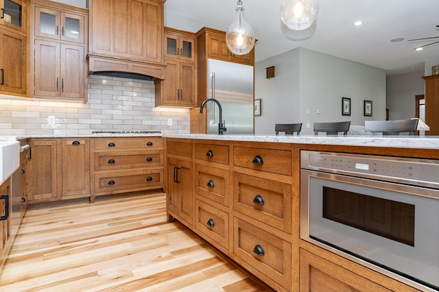 918 Hidden Meadow Ln, Lake City, MN 55041 - kitchen with appliances with stainless steel finishes, brown cabinetry, light countertops, light wood-type flooring, and custom range hood