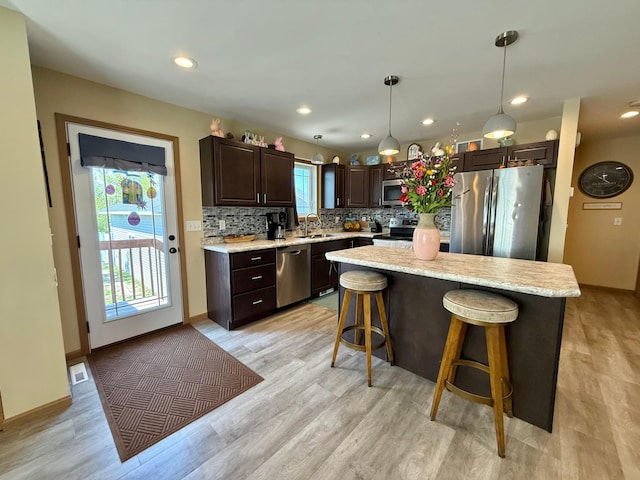 2014 Nelson Dr, Thief River Falls, MN 56701 - kitchen with stainless steel appliances, dark brown cabinetry, a breakfast bar area, tasteful backsplash, and light wood-style floors