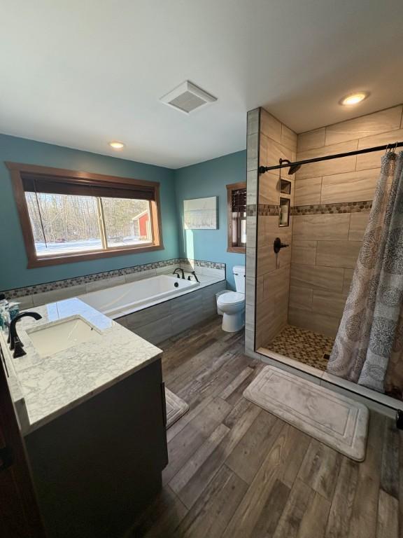 46824 Foss Rd, Osage, MN 56570 - bathroom featuring toilet, a garden tub, a tile shower, wood finished floors, and vanity