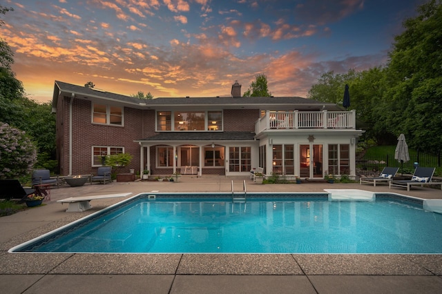 6413 Mendelssohn Ln, Edina, MN 55343 - back of property at dusk with a balcony, a patio area, a chimney, an outdoor pool, and a fire pit