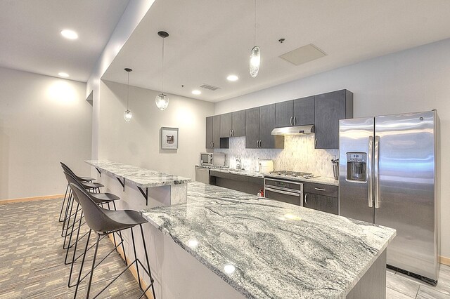 740 Portland Ave Unit 1005, Minneapolis, MN 55415 - kitchen featuring appliances with stainless steel finishes, under cabinet range hood, a breakfast bar, backsplash, and baseboards