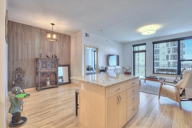 740 Portland Ave Unit 1005, Minneapolis, MN 55415 - kitchen featuring light wood finished floors, light brown cabinetry, light stone counters, a kitchen island, and a breakfast bar