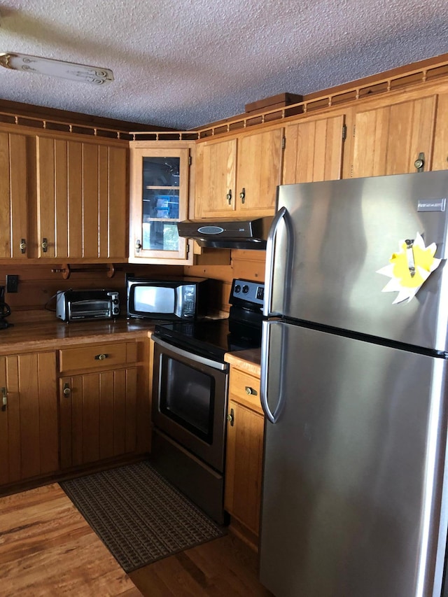 43923 Vista Rd, Isle, MN 56342 - kitchen featuring stainless steel appliances, under cabinet range hood, wood finished floors, a textured ceiling, and brown cabinets
