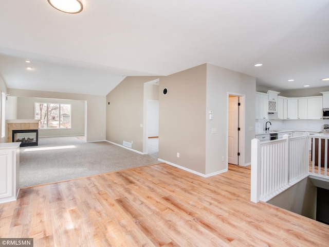 20595 Kearney Path, Lakeville, MN 55044 - unfurnished living room with a sink, light wood-style floors, baseboards, a multi sided fireplace, and lofted ceiling