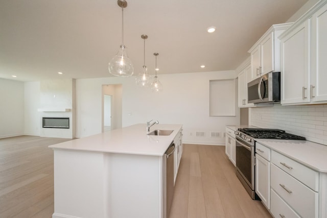 9729 49th St NE, Saint Michael, MN 55376 - kitchen featuring appliances with stainless steel finishes, backsplash, light wood finished floors, a center island with sink, and white cabinetry