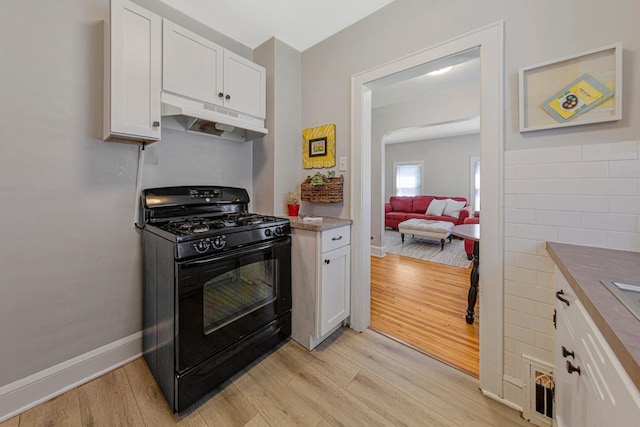 624 2nd St NE, Faribault, MN 55021 - kitchen with black range with gas cooktop, under cabinet range hood, white cabinets, light wood-style flooring, and baseboards