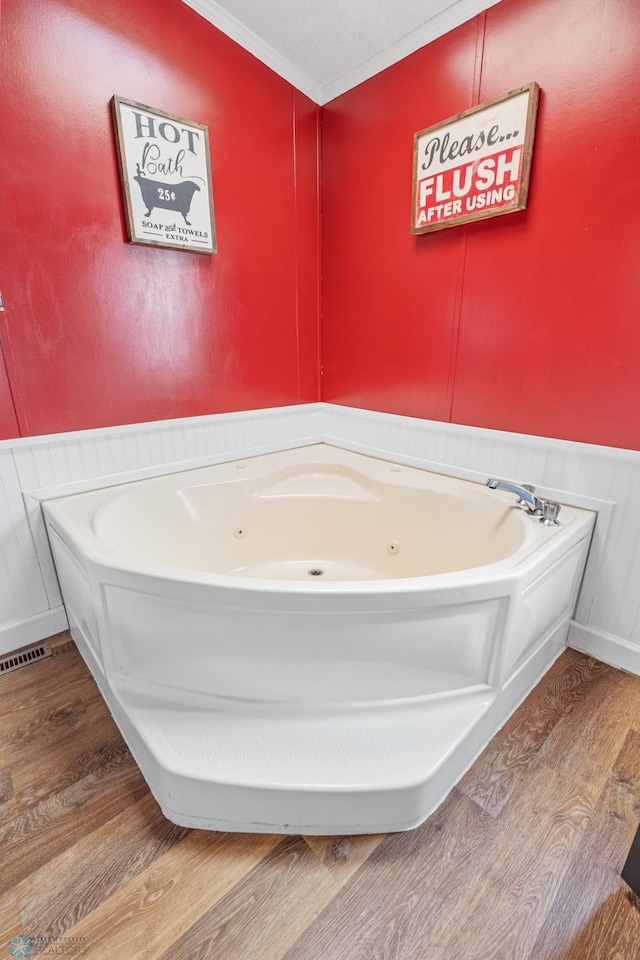 3022 Sandy Beach Rd, Hatton, ND 58240 - bathroom featuring wood finished floors, a tub with jets, a wainscoted wall, a decorative wall, and ornamental molding