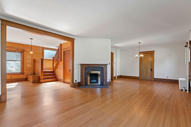 408 5th St E, Northfield, MN 55057 - unfurnished living room featuring light wood-style floors, radiator, a fireplace, stairs, and a chandelier