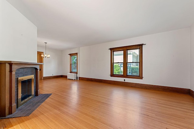 408 5th St E, Northfield, MN 55057 - unfurnished living room with light wood finished floors, radiator, a brick fireplace, a chandelier, and baseboards