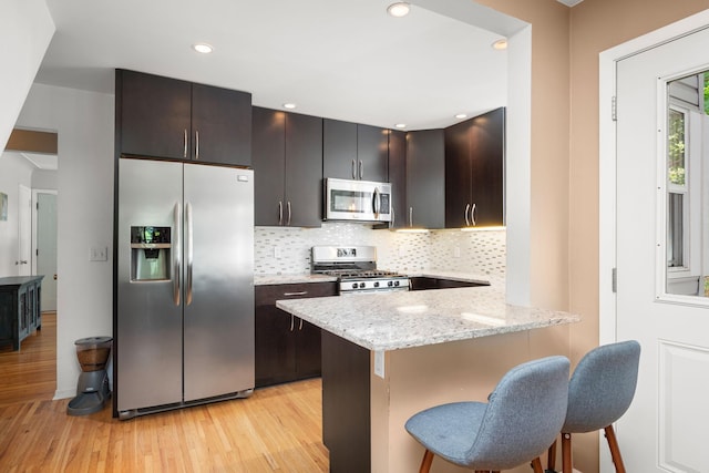 2934 Natchez Ave S, Saint Louis Park, MN 55416 - kitchen with stainless steel appliances, light wood-type flooring, a breakfast bar area, decorative backsplash, and a peninsula