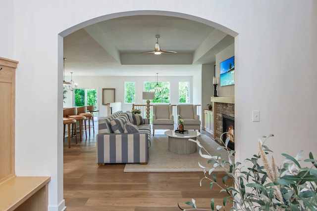 31709 Green Scene Dr, Breezy Point, MN 56472 - living area featuring a ceiling fan, a raised ceiling, wood finished floors, a stone fireplace, and a chandelier