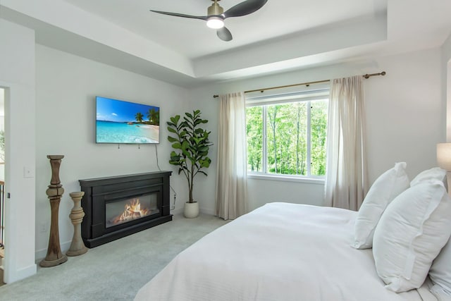 31709 Green Scene Dr, Breezy Point, MN 56472 - bedroom with carpet flooring, a tray ceiling, a glass covered fireplace, ceiling fan, and baseboards