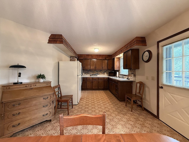 1646 5th St, Montevideo, MN 56265 - kitchen featuring freestanding refrigerator, light countertops, tasteful backsplash, dark brown cabinets, and a textured ceiling