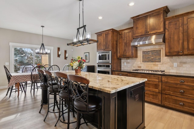 15653 Cobblestone Lake Pkwy, Apple Valley, MN 55124 - kitchen with stainless steel appliances, under cabinet range hood, a center island, backsplash, and light wood-style floors