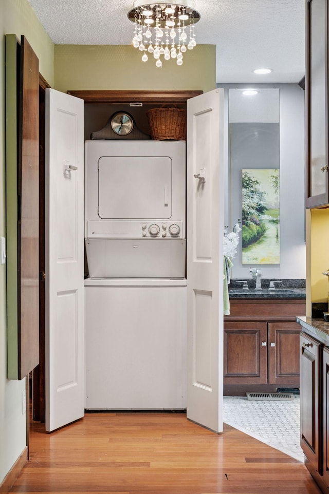 1511 Colleen Ave, Arden Hills, MN 55112 - laundry room featuring estacked washer and dryer, light wood finished floors, a textured ceiling, and a chandelier