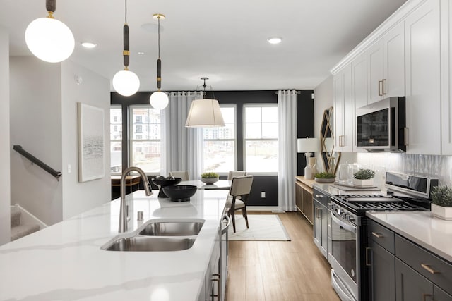 906 Woodlawn Ave Unit D, Saint Paul, MN 55116 - kitchen with appliances with stainless steel finishes, a sink, light wood-style flooring, decorative backsplash, and pendant lighting