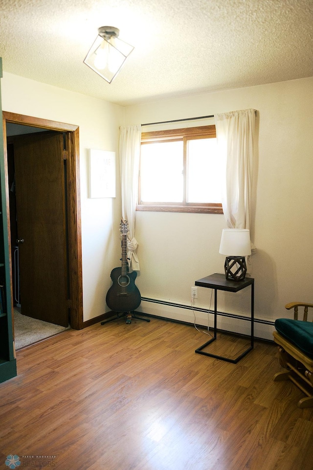 806 E St, Bottineau, ND 58318 - unfurnished room featuring wood finished floors, a baseboard radiator, and a textured ceiling