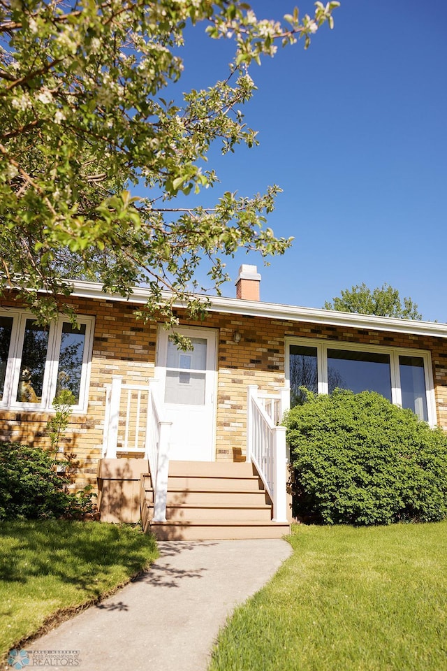 806 E St, Bottineau, ND 58318 - view of front of property with a chimney, a front yard, and brick siding