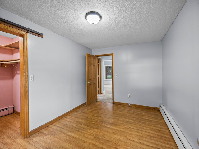 5252 5th St NE, Columbia Heights, MN 55421 - unfurnished bedroom with baseboard heating, light wood finished floors, a textured ceiling, a walk in closet, and a closet