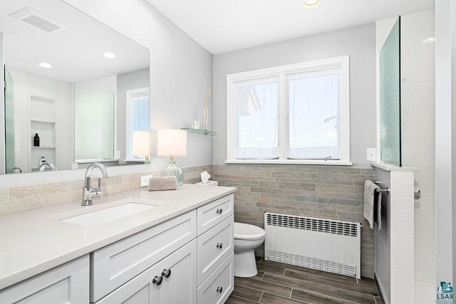2900 London Rd, Duluth, MN 55804 - bathroom with radiator heating unit, vanity, tile walls, toilet, and wood finished floors