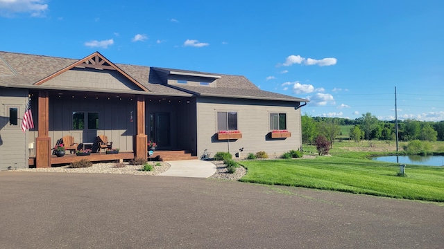 8530 Fir St, Greenfield, MN 55373 - view of front of property with a front lawn, a water view, a porch, a shingled roof, and board and batten siding