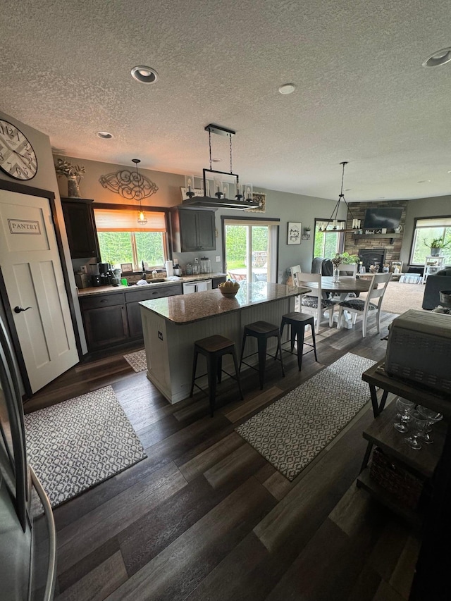 22592 43rd Ave, Saint Augusta, MN 56301 - kitchen featuring a textured ceiling, a kitchen island, dark wood-style floors, decorative light fixtures, and a fireplace