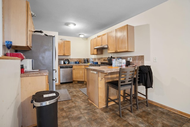1599 Rice St, Saint Paul, MN 55117 - kitchen with appliances with stainless steel finishes, light brown cabinetry, a peninsula, and under cabinet range hood