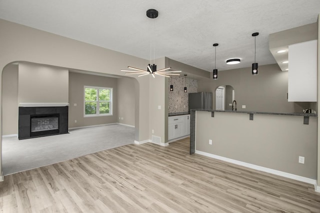 7658 Silver Lake Rd, Mounds View, MN 55112 - unfurnished living room with arched walkways, light wood-type flooring, ceiling fan, baseboards, and a tiled fireplace
