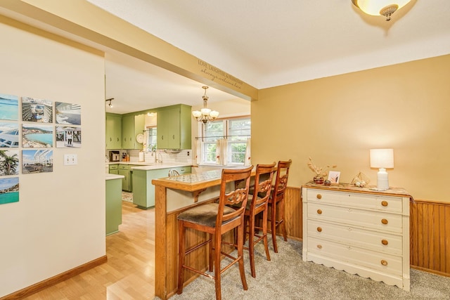 2816 29th Ave NE, Saint Anthony, MN 55418 - kitchen with green cabinetry, a chandelier, wainscoting, a kitchen breakfast bar, and light countertops